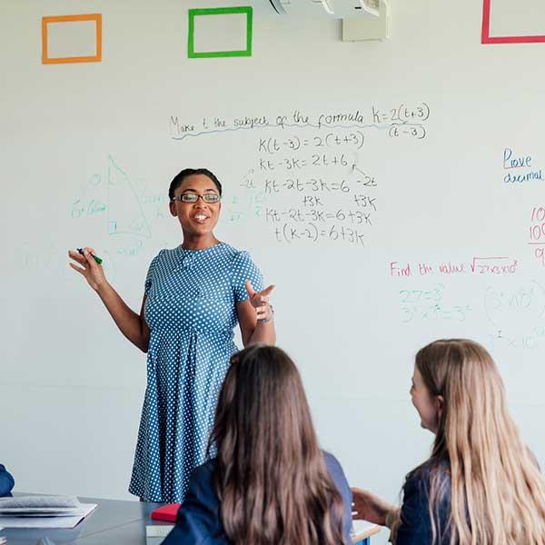 Teacher standing at whiteboard teaching secondary pupils