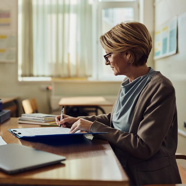 Mature female teacher grading exam papers at high school.