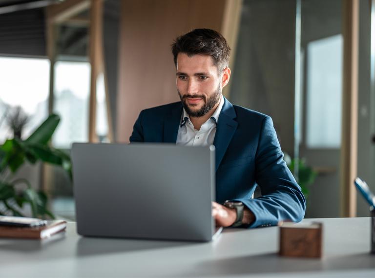 A Caucasian male businessman engages with a laptop while dressed in formal attire, conveying productivity within an office setting.