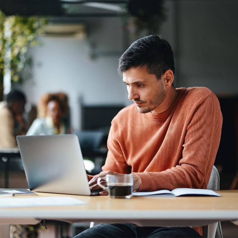 A serious Caucasian entrepreneur typing on his laptop while sitting at the office desk.