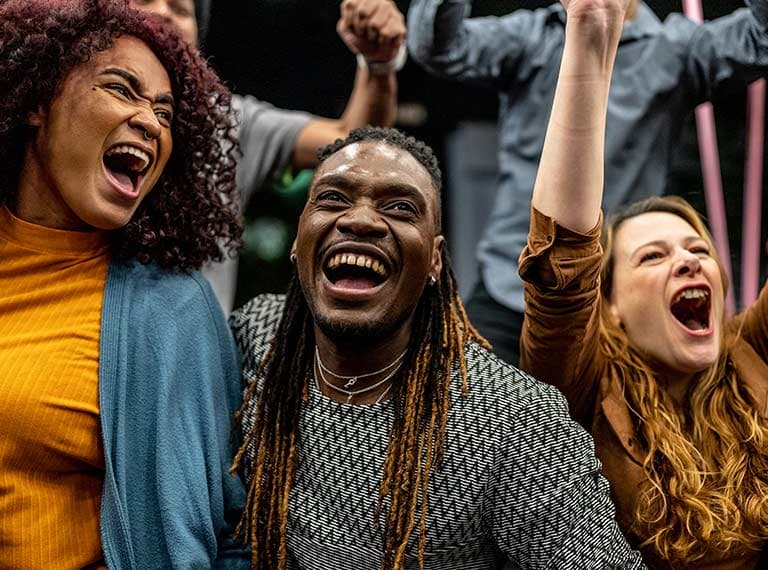 Diverse group of people cheering with raised fists, expressing joy and celebration with wide smiles and enthusiastic energy.