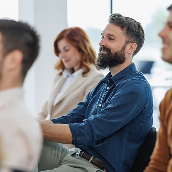 Bearded man in blue shirt smiling during a group meeting with colleagues in a bright office setting