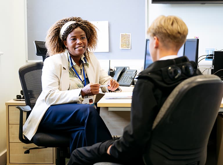 Female healthcare professional in white coat with blue lanyard consulting with patient at desk in medical office