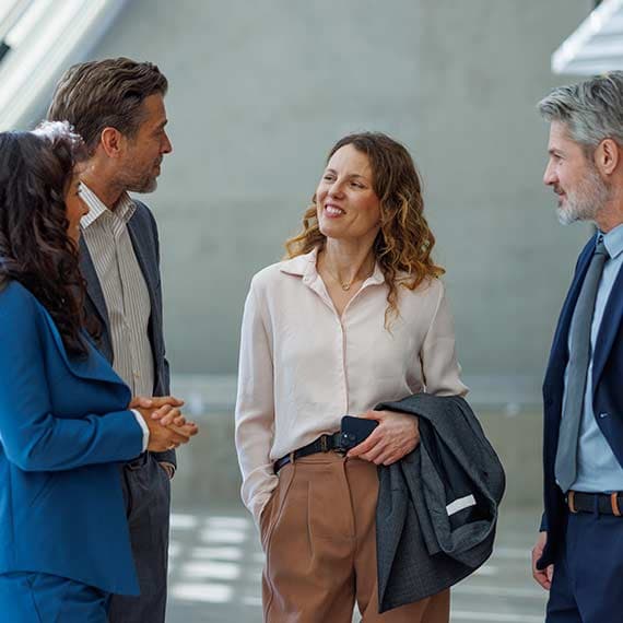 Four business professionals having a friendly conversation in a modern office setting with natural light.