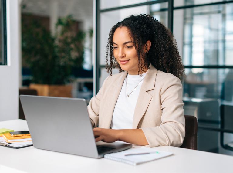 Woman uses laptop. Successful curly haired Hispanic or Brazilian woman in stylish elegant clothes, office employee, secretary or hr manager, using a laptop while sitting at her workplace, working.