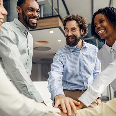Diverse business team putting hands together in office huddle, smiling and showing teamwork and collaboration.