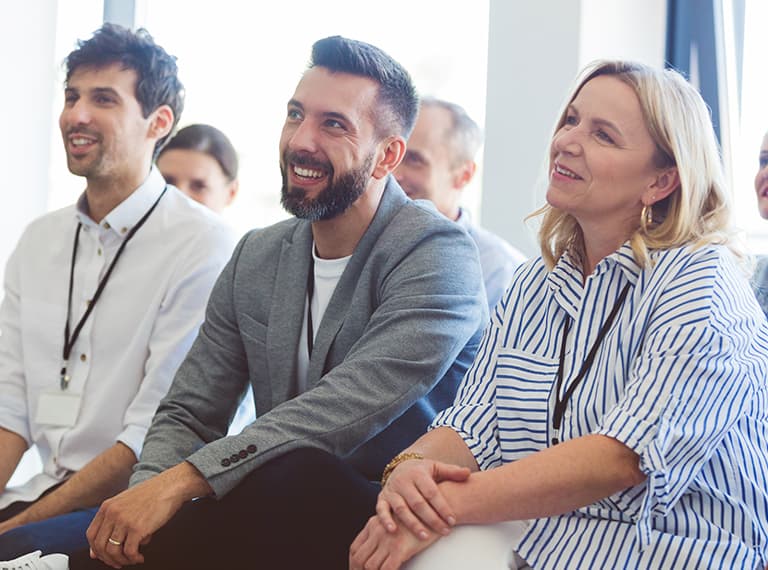 Three smiling professionals sitting in a bright conference room, attentively listening during a business presentation.