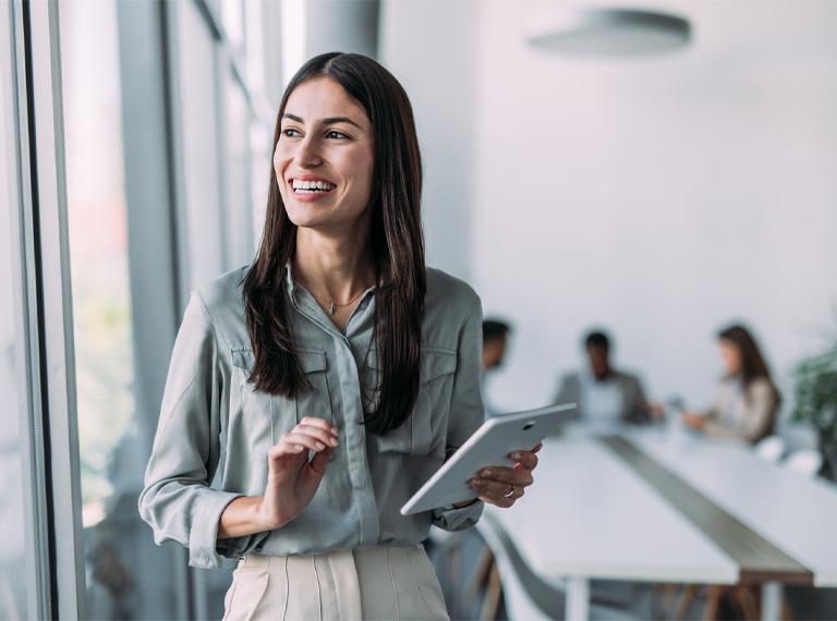 Shot of a smiling businesswoman standing in front of her team and using digital tablet. Portrait of successful businesswoman standing with her colleagues working in background.