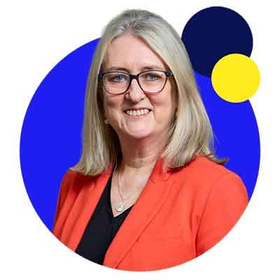 Woman with gray hair and glasses wearing orange blazer, smiling against blue circular background with yellow accent.