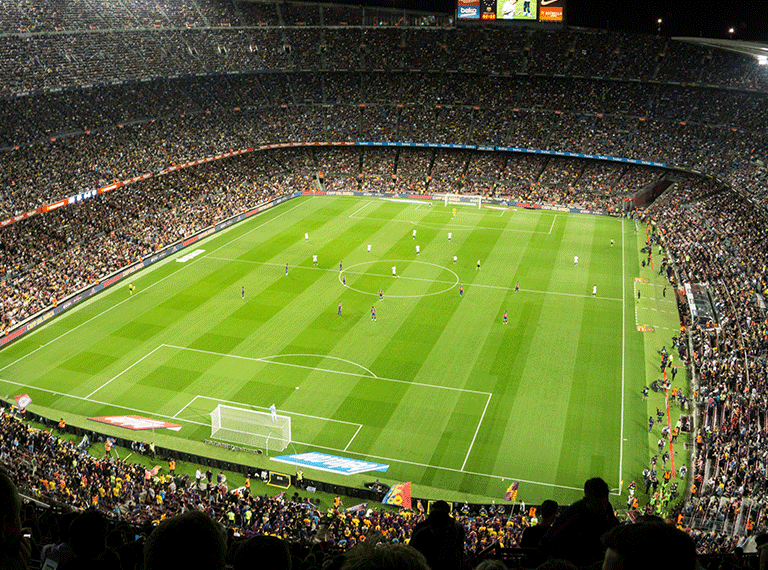 Aerial view of a packed World Cup football stadium at night with bright green striped field and players during a match.