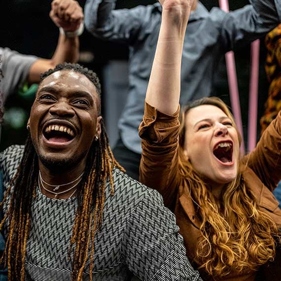 Diverse group of people cheering with raised fists, expressing joy and celebration with enthusiastic smiles.
