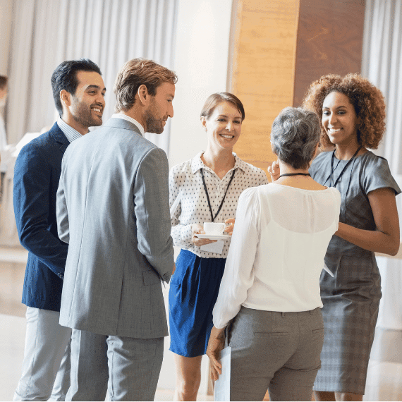 Five diverse professionals standing in a circle having a friendly conversation in a bright modern office space.