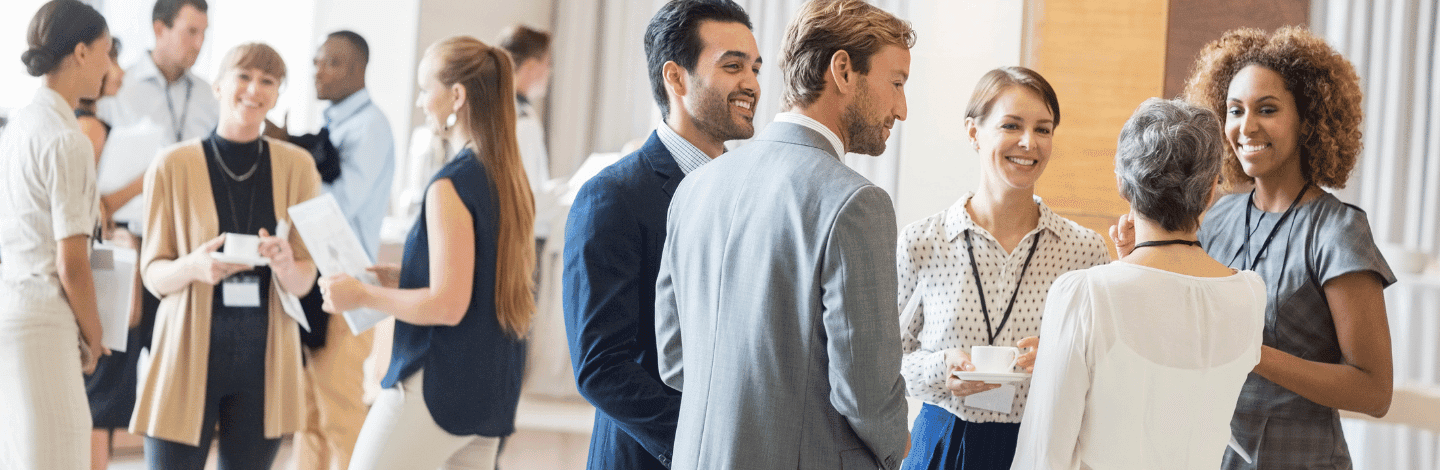 Diverse group of professionals networking and conversing at a business event in a bright, modern venue.